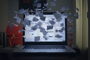 Overwhelmed laptop screen displaying messy tabs and unread emails in a cluttered workspace filled with scattered notes. A laptop screen is cluttered with numerous open browser tabs and unread emails, surrounded by a chaotic workspace. Papers are strewn about, highlighting a busy moment in digital AI generated