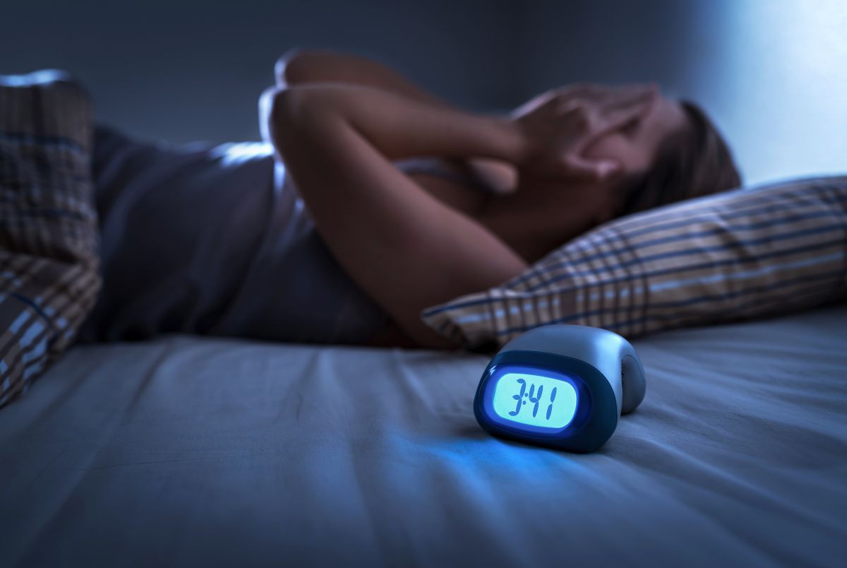 Woman with trouble sleeping and bright alarm clock