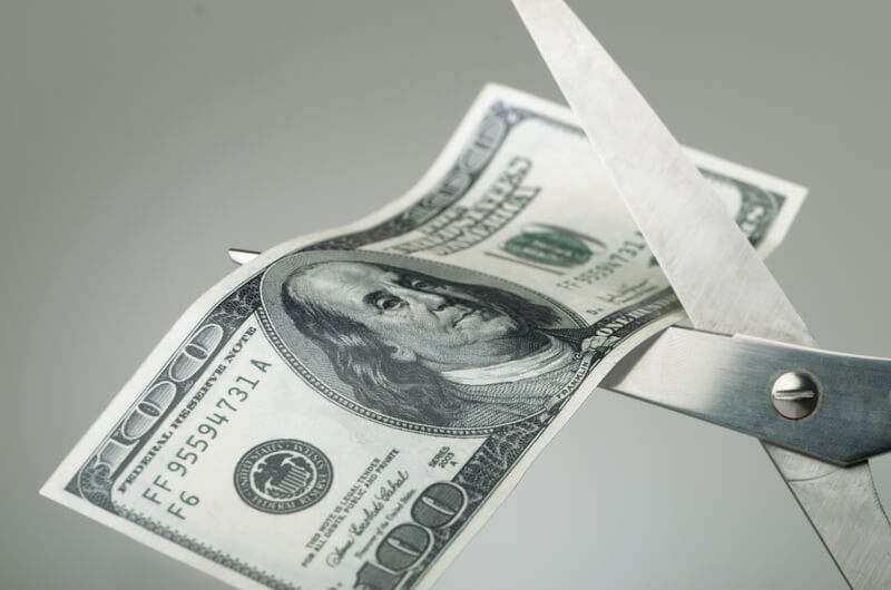 Scissors cutting a dollar bill in half. Money being cut showing cutbacks or wasteful spending