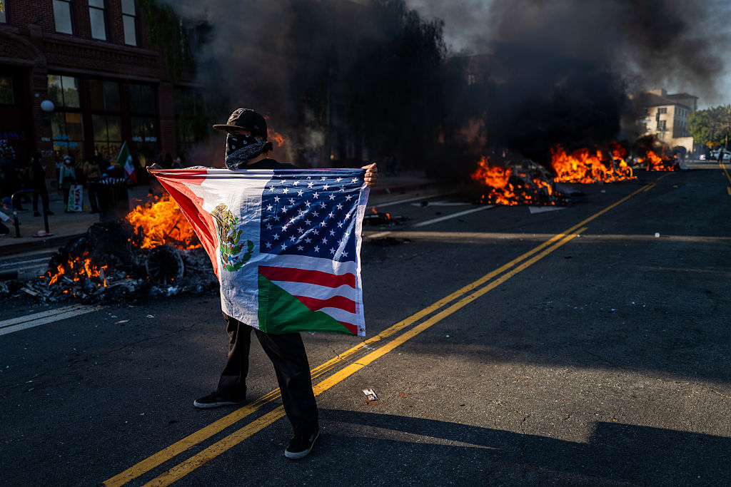 LOS ANGELES, CALIFORNIA - JUNE 08: A protester holds up a joint United States and Mexico flag during protests after a series of immigration raids on June 08, 2025 in Los Angeles, California. Tensions in the city remain high after the Trump administration called in the National Guard against the wishes of city leaders. (Photo by Spencer Platt/Getty Images)