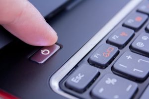 A finger is pushing the power button to wake laptop up