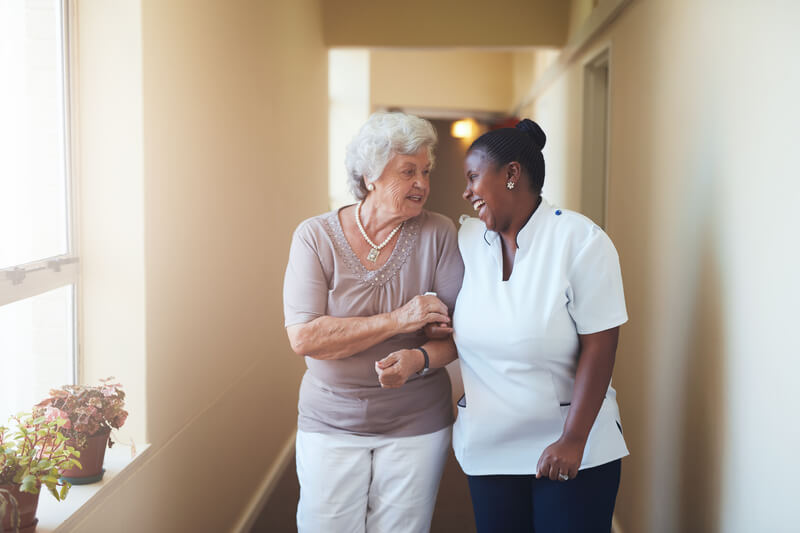 Smiling caregiver puts arm around her smiling senior family member