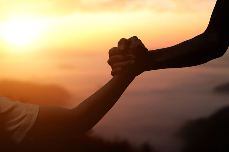 Silhouette of giving a helping hand, hope and support each other over sunset background