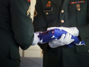 Military Honor Guard Folds United States Flag at V. This military honor guard carefully folds the United States flag for presentation to family members at a veterans funeral. Selective focus on flag and gloved hands. Would make good illustration for U. S. Veterans Day, U. Memorial Day or honoring military service.
