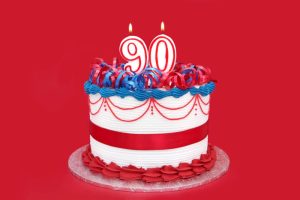90th cake with numeral candles, on vibrant red background.