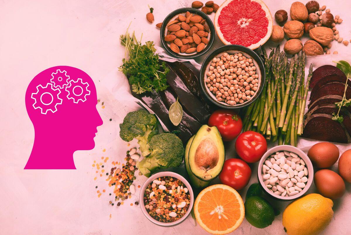 Brain health concept with pink head and gears icon next to a variety of brain-boosting foods including vegetables, fruits, legumes, nuts, and eggs