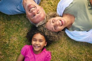 Looking Down On Multi Racial Grandparents With Granddaughter Lying Outdoors On Grass