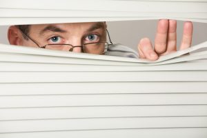 Man taking a sneak peek of medicare plans. Close-up of venetian blind with male looking out of it
