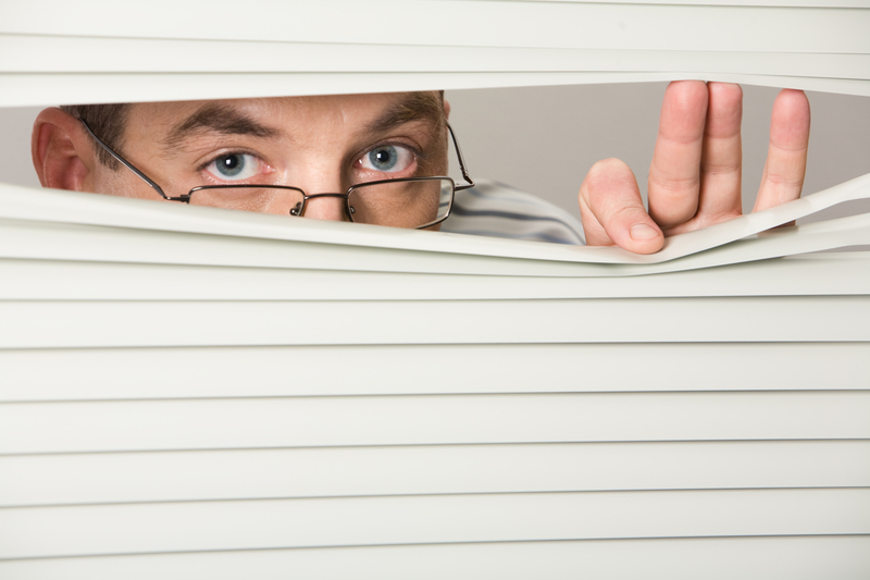 Man taking a sneak peek of medicare plans. Close-up of venetian blind with male looking out of it