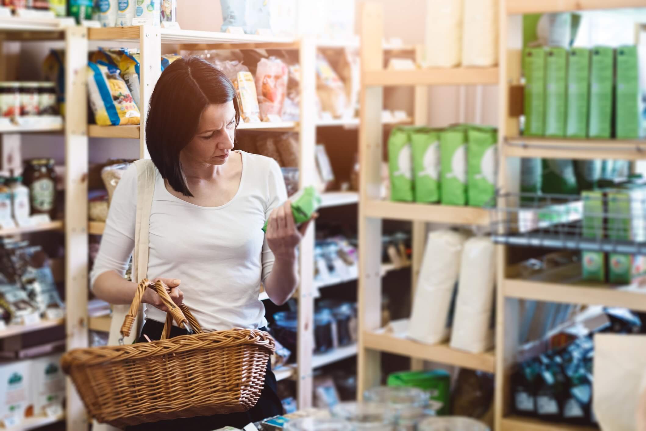 Woman reading product information on label. Woman choosing products in ecological shop with healthy food and reading product information on label