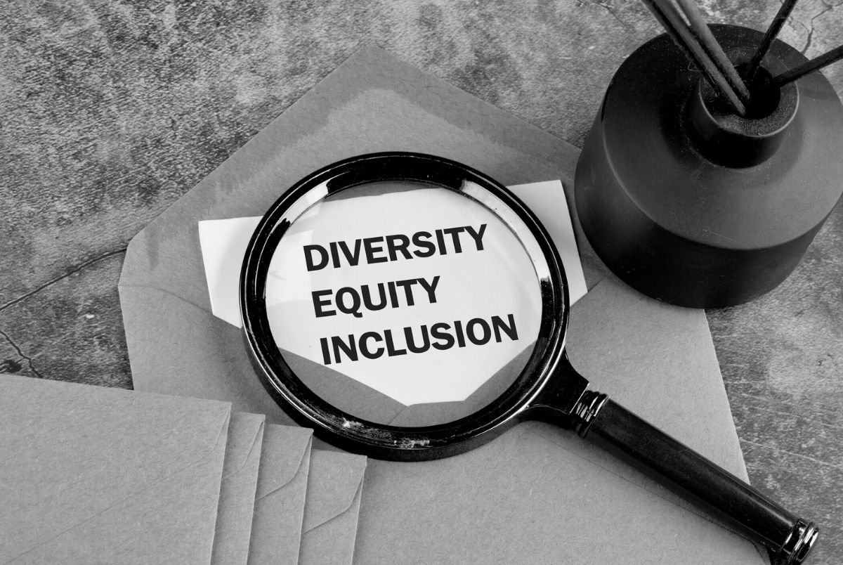 Diversity, equity, inclusion DEI symbol. Words DEI, diversity, equity, inclusion appearing on a blank sheet peeking out of an envelope through a magnifying glass, a conceptual black and white photo.