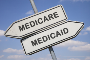 Two white direction signs with arrows and the words medicare and medicaid. Dual eligible monthly enrollment option.