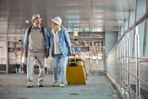 Two happy senior travelers walking hand in hand. Full-length portrait of a pleased female tourist with a trolley suitcase smiling at her husband