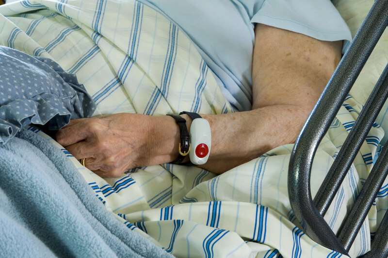 Elderly Health Care. View of elderly person s arm in raised hospital bed with emergency notification wrist device.