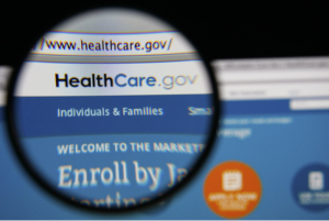 Photo of HealthCare.gov Marketplace insurance homepage on a monitor screen through a magnifying glass.