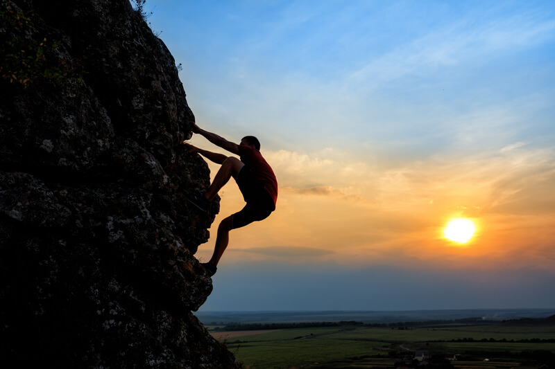 Young man climbing the mountain ridge on sunset