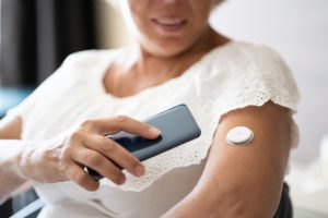 Woman Testing Glucose Level With Continuous Glucose Monitor On Mobile Phone. Diabetes care.
