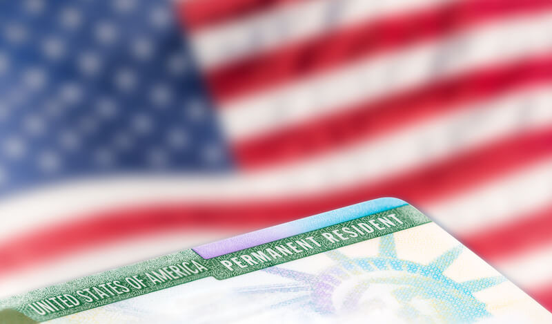American permanent resident card, immigration concept. United States of America permanent resident card, green card, with US flag in the background. Legal immigration concept.