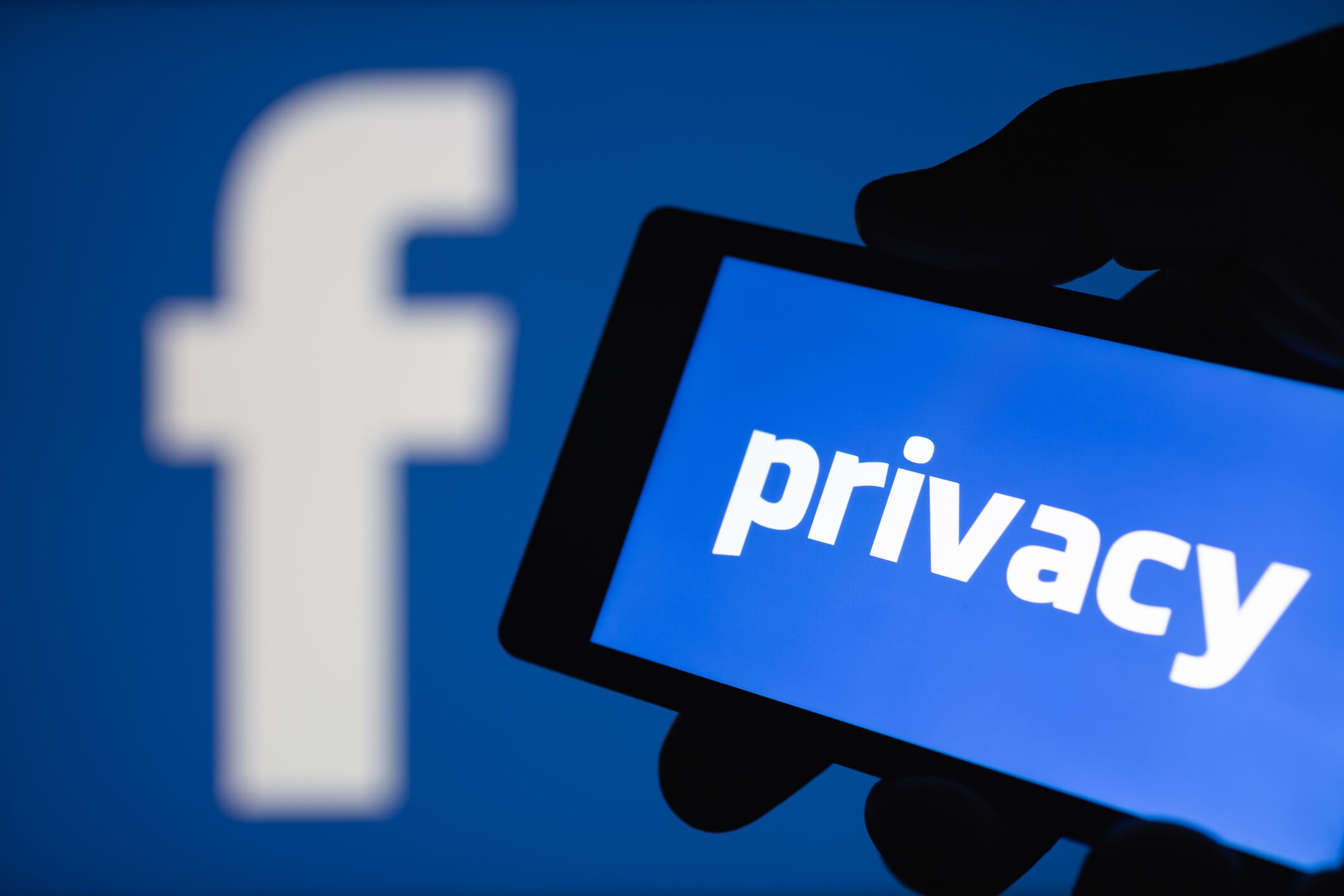 MOSCOW, RUSSIA - September 14, 2018: A smartphone in hand displaying the privacy text. Logo of the Facebook blurred on background. The concept of privacy on popular social network. Shallow DOF