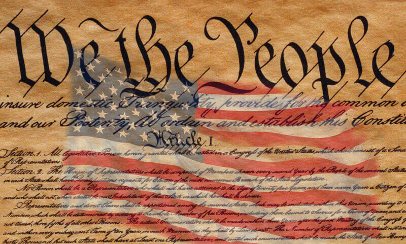 This is the preamble to the U. S. Constitution that starts with the words, we the people. An American flag is digitally composited into the center of the preamble to the U. Constitution. This is a digitally created image.