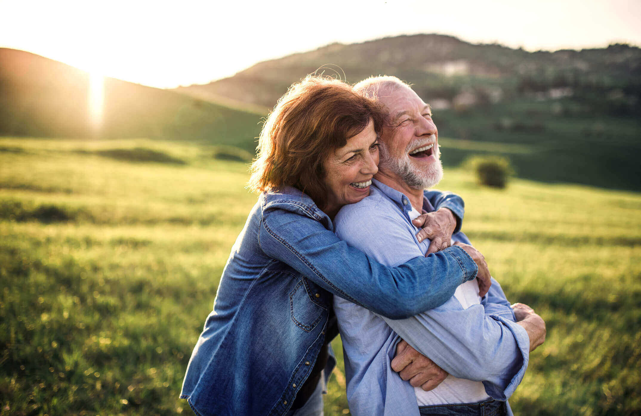 Side view of senior couple hugging outside in spring nature at sunset. Happy senior couple outside in spring nature, hugging at sunset. Side view.
