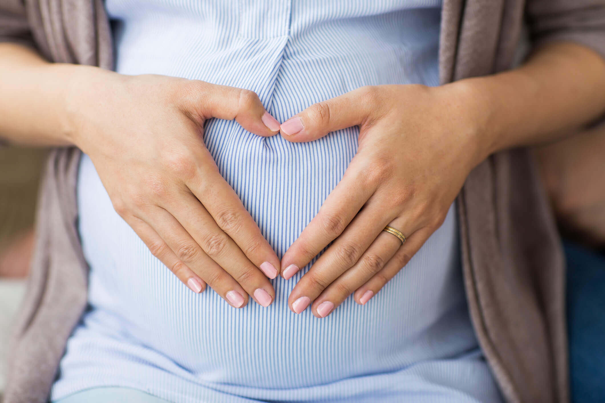 Close up of pregnant woman making heart on belly. Pregnancy, love and people concept - close up of pregnant woman making hand heart on belly