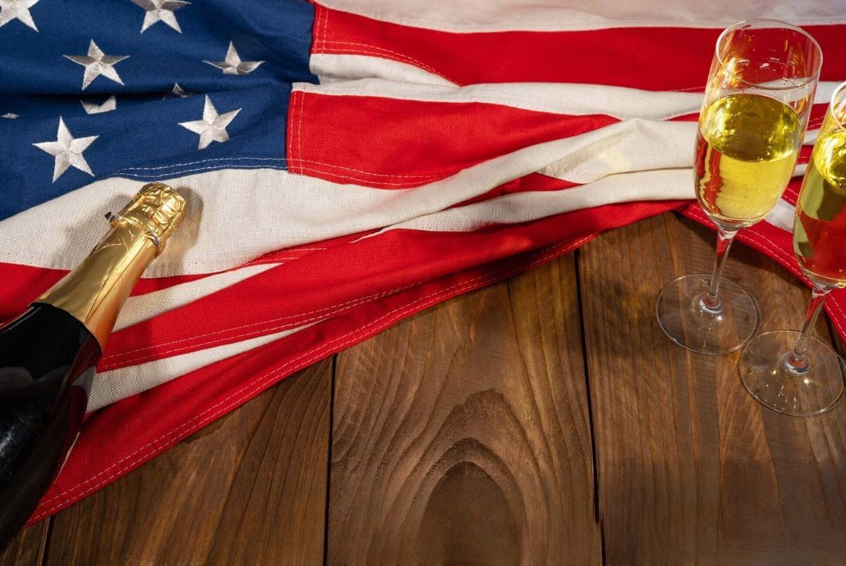 Happy New Year, New Year s Eve Sylvester or other holiday greeting card, celebration background USA - American flag, sparkling wine or champagne bottle and glasses on wooden table, top view