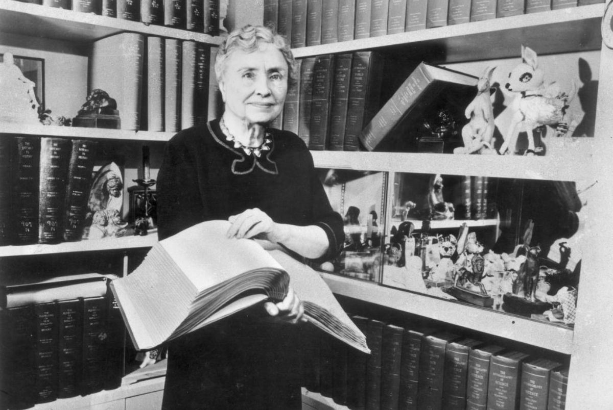 1956: Portrait of American writer, educator and advocate for the disabled Helen Keller (1880 - 1968) holding a Braille volume and surrounded by shelves containing books and decorative figurines. A childhood illness left Keller blind, deaf and mute. (Photo by Hulton Archive/Getty Images)