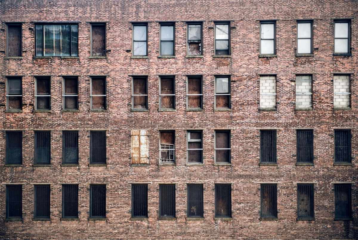 Front view of a boarded-up abandoned brick skyscraper building windows from the street in New York City.