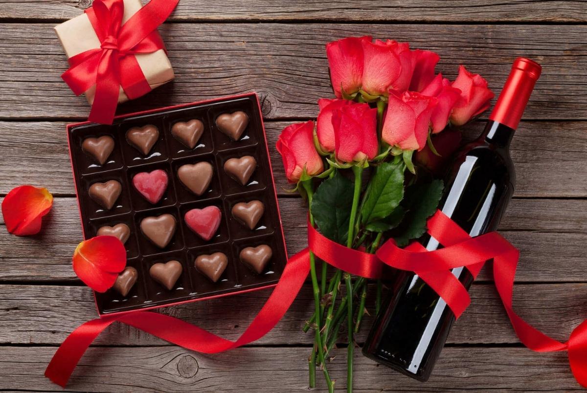 Valentines day with red roses, wine bottle and chocolate box on wooden table. Top view