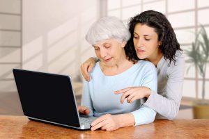 Young woman doctrine teaches daughter of an elderly woman laptop computer. Young women doctrine teaches daughter of an elderly women how to work using laptop computer at home