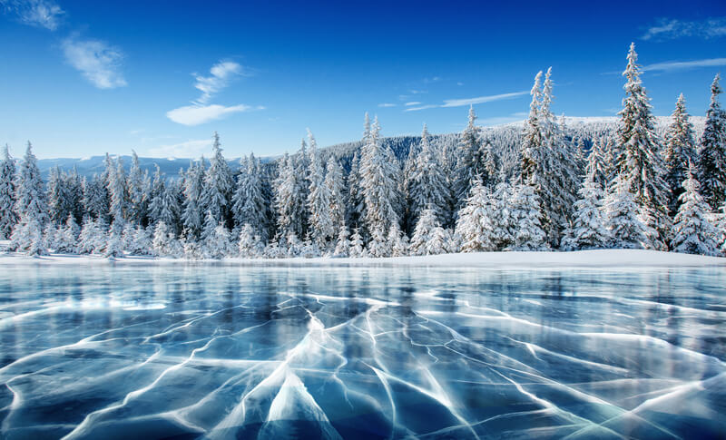 Blue ice and cracks on the surface of the ice. Frozen lake under a blue sky in the winter. The hills of pines. Winter. Carpathian, Ukraine, Europe