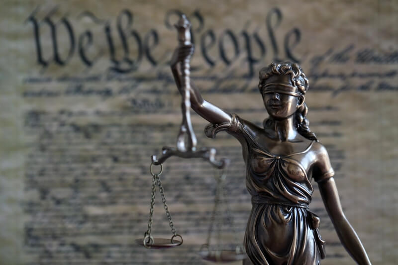 Dark scene with Lady Justice and background of blurred US Constitution page close up. Lawsuit and judgement in United States of America