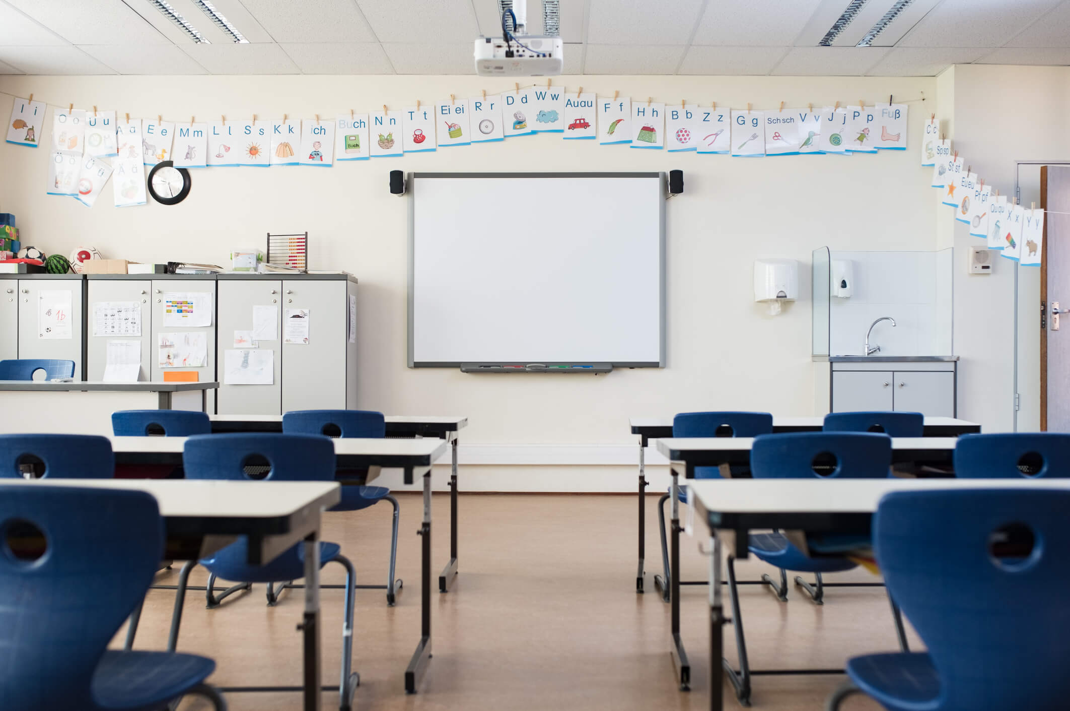 Empty classroom with whiteboard. School desk and chairs in empty modern classroom. Empty class room with white board and projector in elementary school. Primary classroom with smartboard and alphabet on wall.