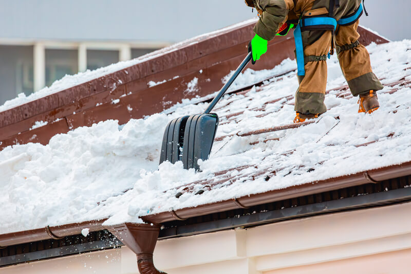 Communal services worker industrial climber removes snow from the building roof in winter.