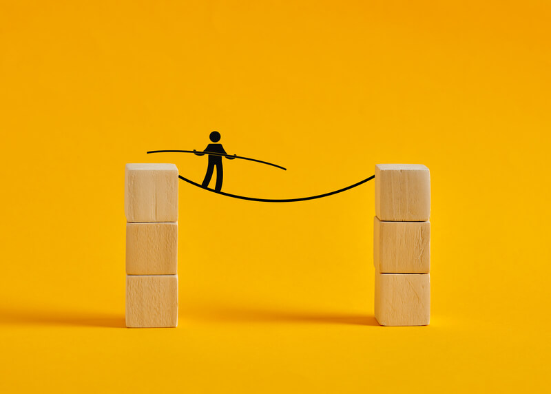 Businessman walking a tightrope between two stacks of blocks. Businessman balancing on a tightrope between two stacks of wooden blocks, representing risk taking, challenge, and overcoming obstacles in business