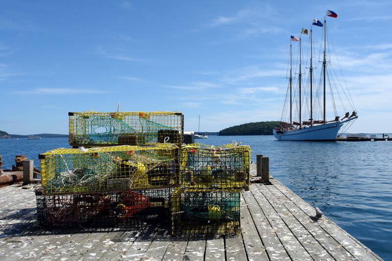 Lobster Traps on a Dock in Maine Fishing Port. Lobster pot traps on a dock in a Maine fishing port with tall ship sailing on water