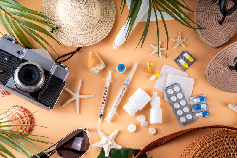 Summer holiday travel background including medications and vacation accessories. Summer holiday travel setup background including first aid kit with medications, pills, hat, and vacation accessories. Medication in journey, vaccinations, travel health insurance concept
