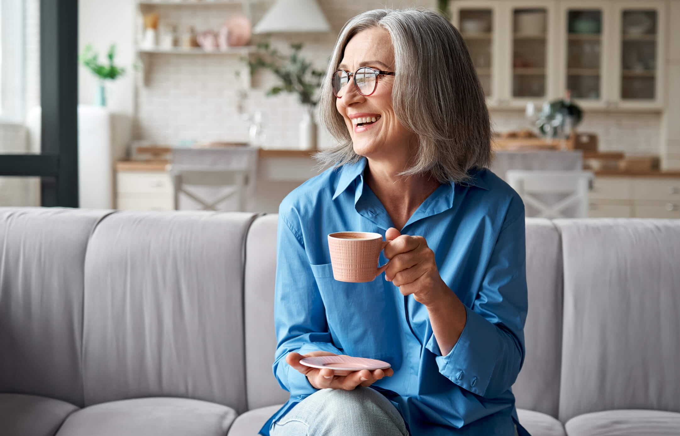 Happy relaxed mature older woman drinking coffee relaxing on sofa at home. Happy beautiful relaxed mature older adult grey-haired woman drinking coffee relaxing on sofa at home. Smiling stylish middle aged 60s lady enjoying resting sitting on couch in modern living room.
