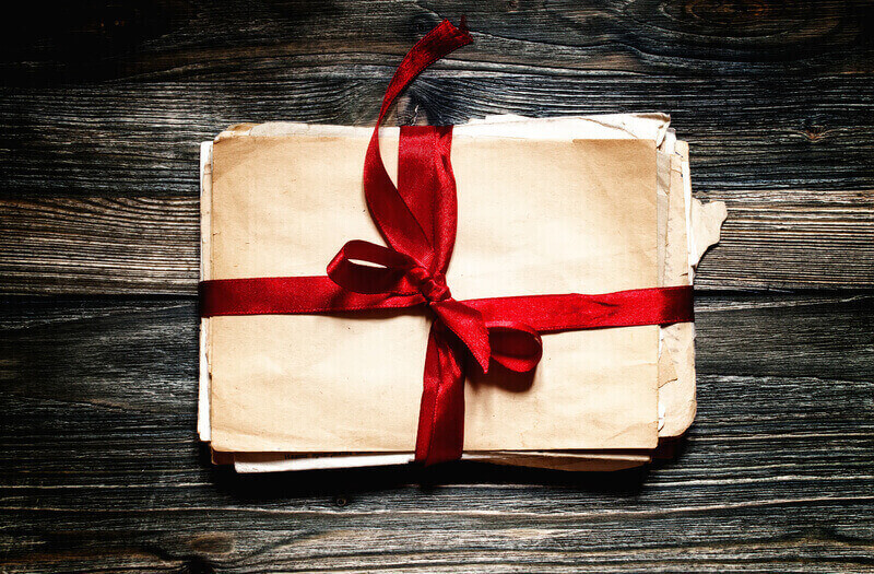 Old letters, tied with a red ribbon on an old wooden background, top view, vintage toned image
