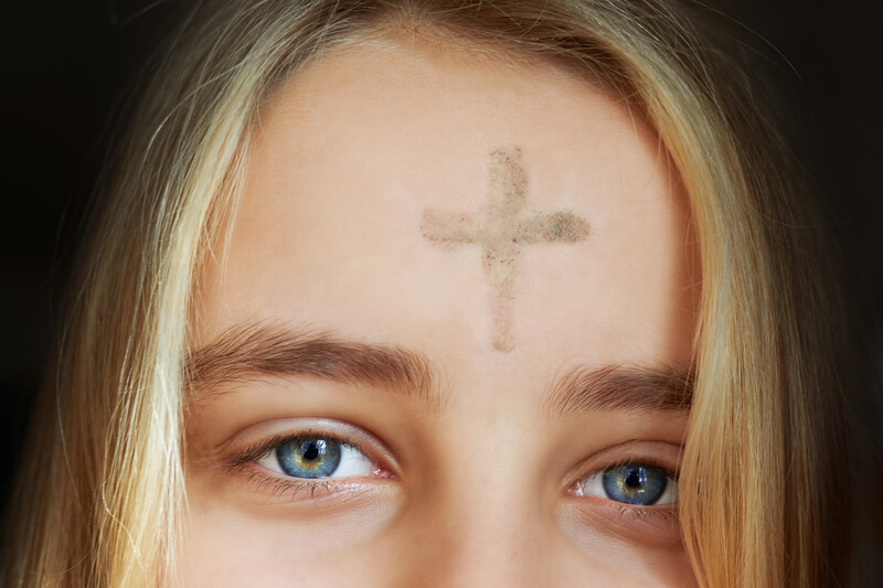 Girl with cross made from ash on forehead. Ash wednesday concept.