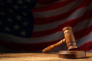 Judge`s gavel on wooden table against American flag in darkness, space for text. Judge s gavel on wooden table against American flag in darkness