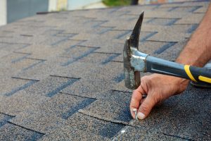 Worker hands installing bitumen roof shingles. Worker Hammer in Nails on the Roof. Roofer is hammering a Nail in the Roof Shingles. Unfinished roof
