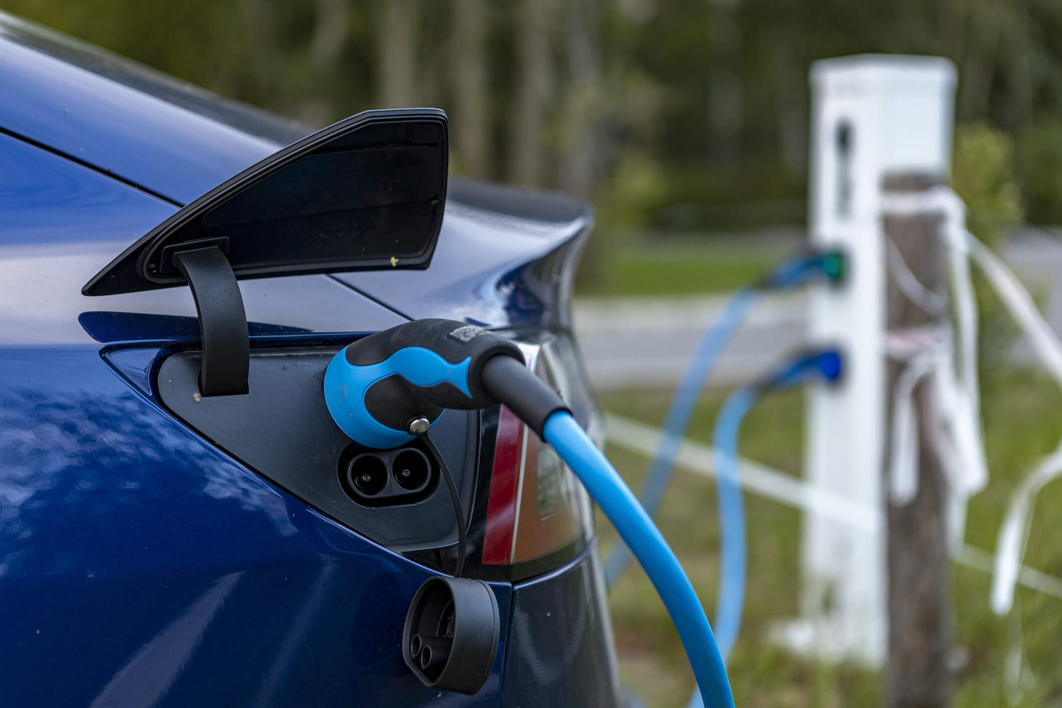 HOGE HEXEL, NETHERLANDS - Aug 30, 2020: Tesla electric car on charging station. HOGE HEXEL, NETHERLANDS - Aug 30, 2020: Closeup of modern design electric Tesla car charging in parking lot with electric cable leading to charge station visible in the background