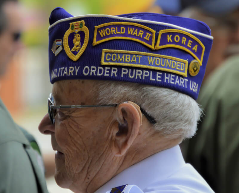 Veteran Wears Decorative Hat with Patches. WWII and Korean War veteran proudly wears a hat with patches displaying his military service: combat wounded, purple heart.