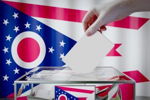 Ohio flag, hand dropping ballot card into a box