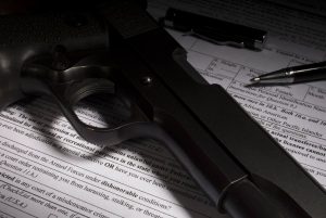 NICS check question on dishonorable discharge. Gun and pen on firearm purchase paperwork with dishonorable discharge question highlighted