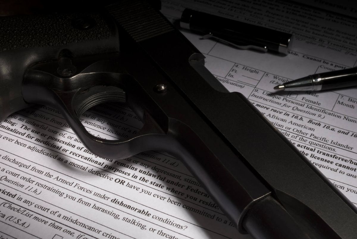 NICS check question on dishonorable discharge. Gun and pen on firearm purchase paperwork with dishonorable discharge question highlighted