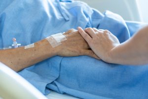 Caregiver holding elderly senior patient ageing old adult person hand in hospital bed or nursing hospice, geriatrician palliative home, while caretaker having medical health care service.