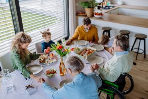 A multi-generational family pausing for a moment of prayer or reflection before sharing a meal together at a dining table.